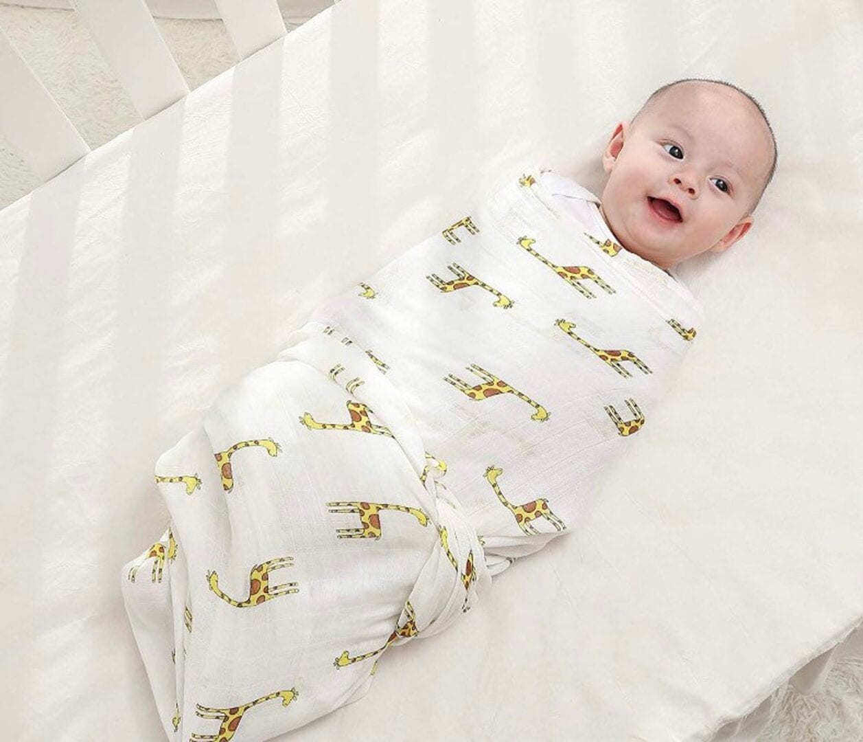Baby wrapped in a white swaddle blanket with cute giraffe pattern