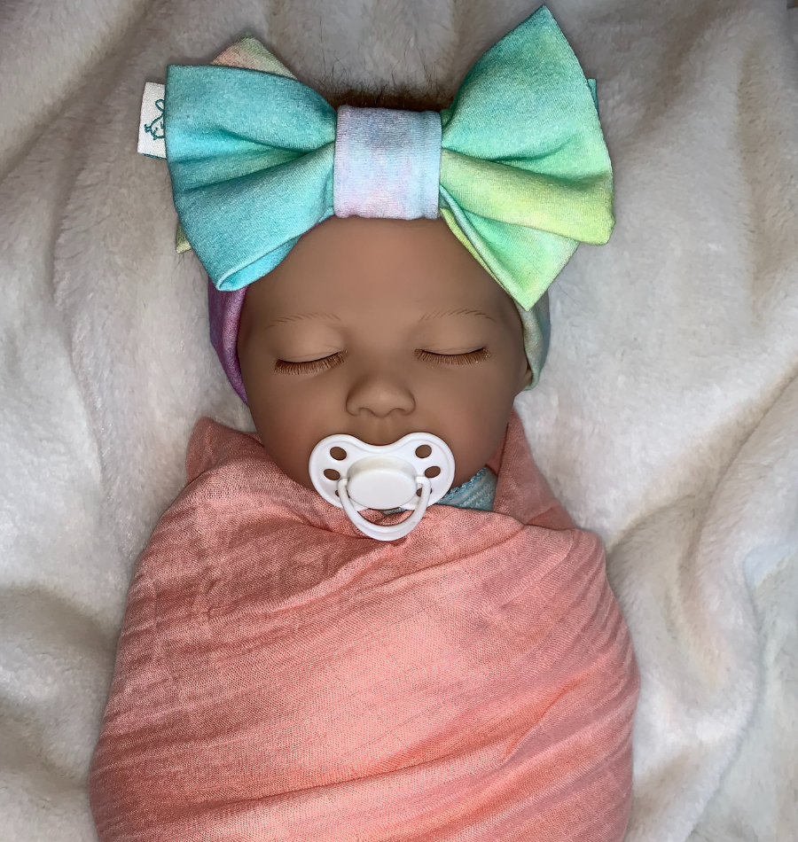 Pretty baby girl wrapped in pink swaddle blanket with pretty little blue green and pink tie dye hair bow headband
